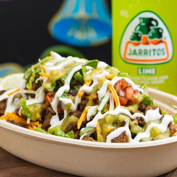 A Sombrero Tacoria burrito bowl with meat, lettuce, cheese, salsa, and sour cream, next to a Jarritos soda.