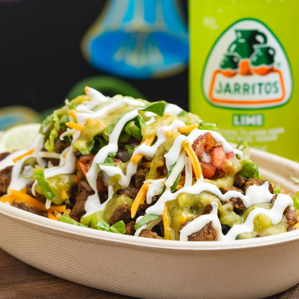 A Sombrero Tacoria burrito bowl with meat, lettuce, cheese, salsa, and sour cream, next to a Jarritos soda.