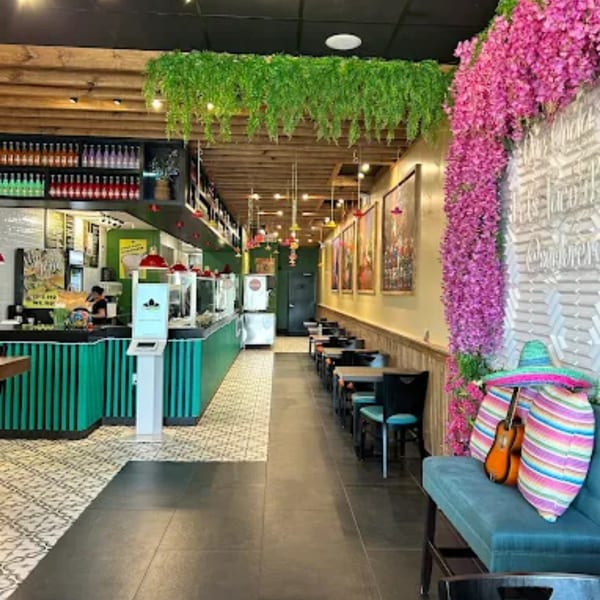 Vibrant Mexican restaurant interior with a long counter, dining tables, and colorful floral decorations.
