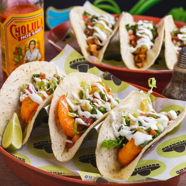 Three shrimp tacos with lime, hot sauce, and a pepper grinder on a red tray.