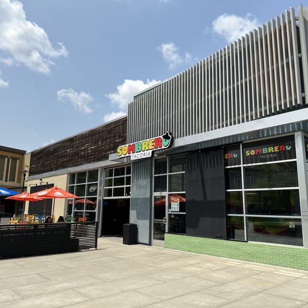 Exterior of Sombrero Tacoria with outdoor seating under red umbrellas on a sunny day.
