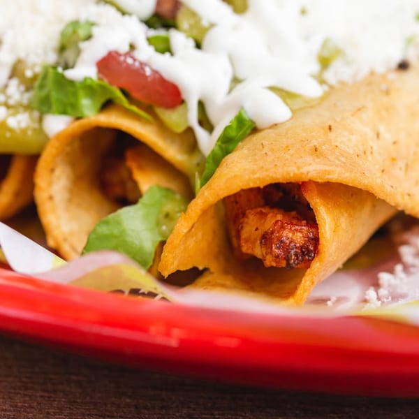 Crispy taquitos filled with meat, topped with lettuce, tomatoes, cheese, and sour cream.