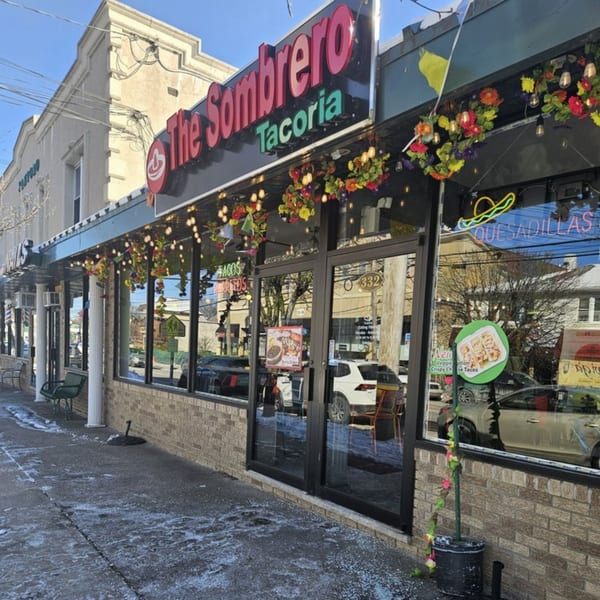 The Sombrero Tacoria storefront with a brick facade, large windows, and colorful floral decorations.