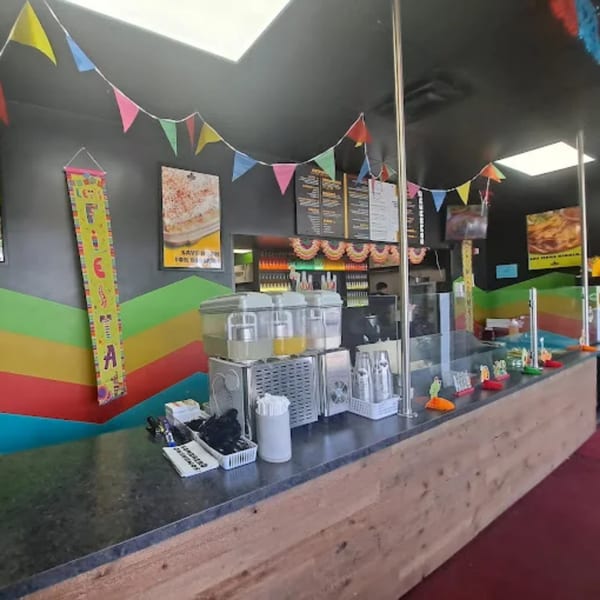 Colorful restaurant interior with a long counter, drink dispensers, and festive decorations.