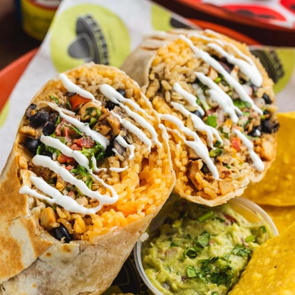 Two burritos with rice, beans, and sour cream, alongside guacamole and tortilla chips.