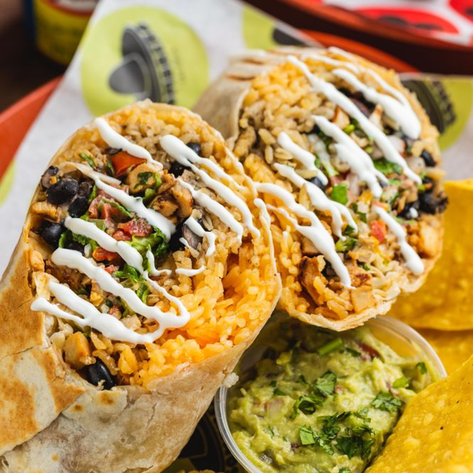 Two burritos with rice, beans, and sour cream, alongside guacamole and tortilla chips.