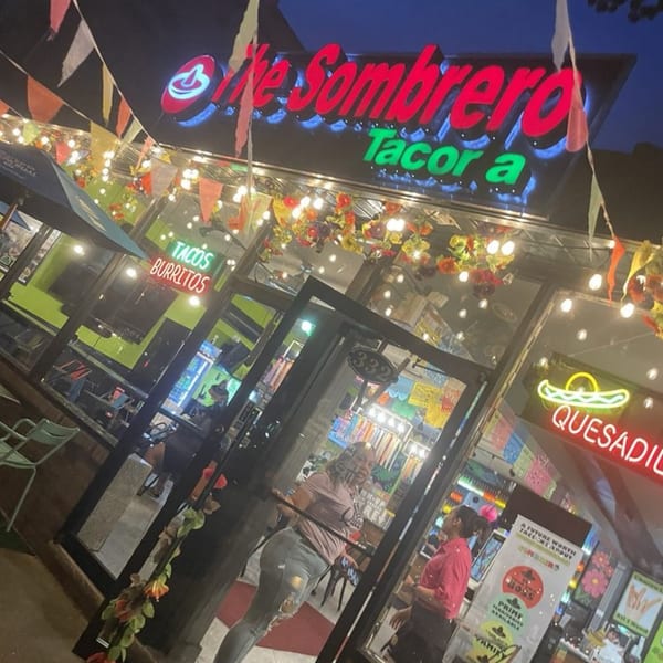 The illuminated exterior of "El Sombrero Taco" restaurant at night, with colorful decorations and neon signs.